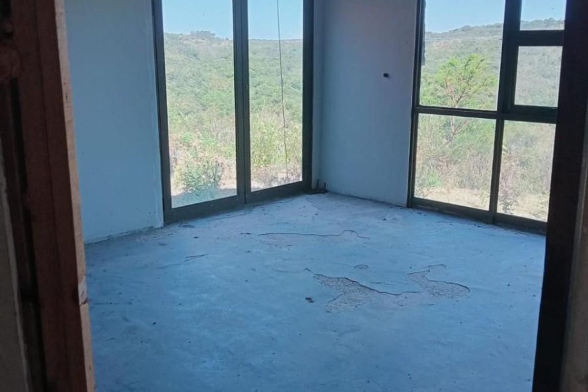 An unfinished bedroom space featuring exposed ceiling beams, large glass sliding doors, and expansive views of the surrounding landscape.