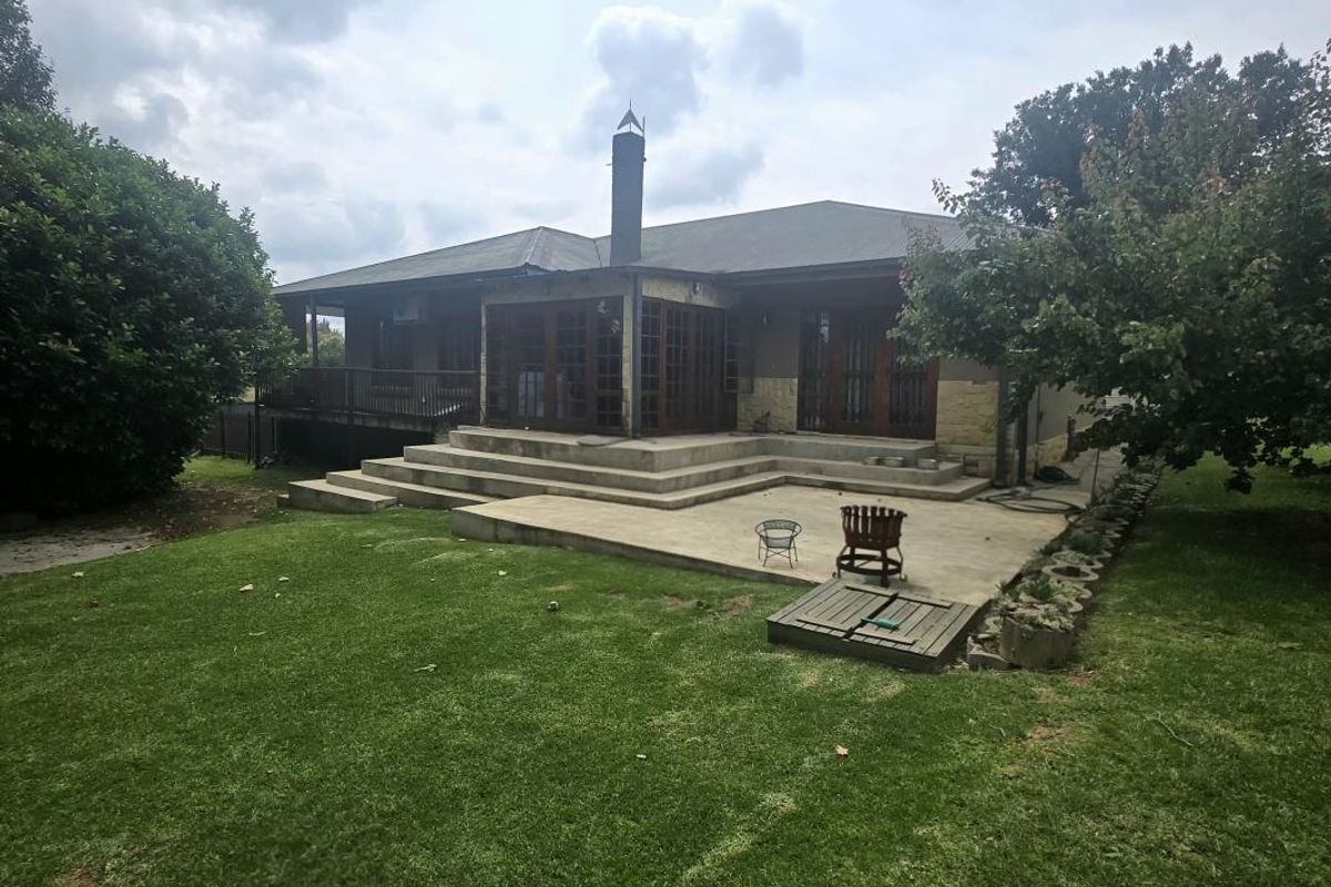 Rear view of the property featuring a concrete patio, raised timber deck, and stone-clad exterior walls with large timber-framed glass doors.
