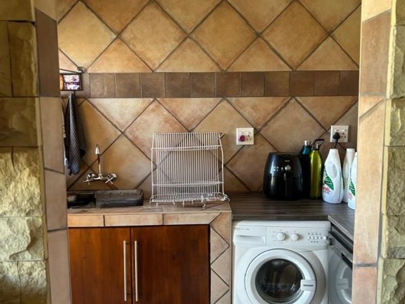 A functional laundry area featuring built-in cabinetry, a sink, and tiled splashbacks, framed by a decorative stone-clad doorway.