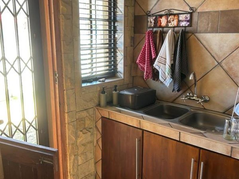 A functional laundry area featuring a double basin sink, wooden cabinetry, and stone-clad walls with direct access to the exterior.