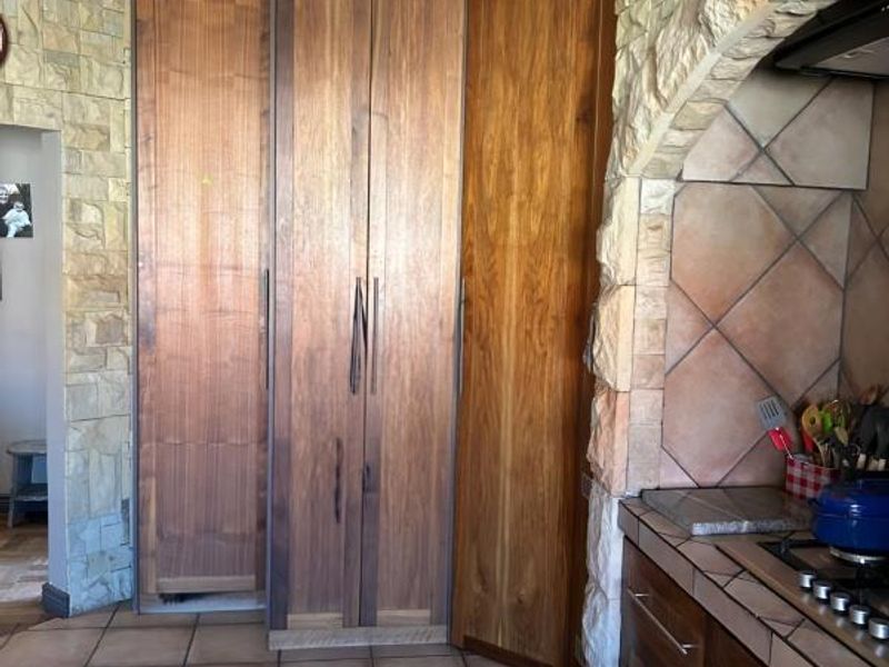 A rustic kitchen featuring custom wood cabinetry, stone-clad walls, tiled flooring, and a built-in gas hob with an integrated extractor fan.