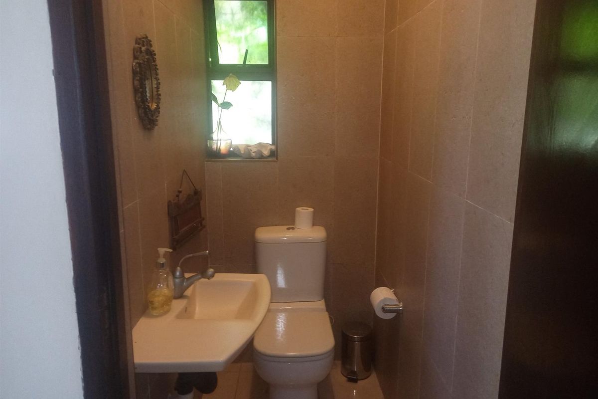 A compact bathroom featuring tiled walls, a wall-mounted basin, and a standard toilet, illuminated by a small window.