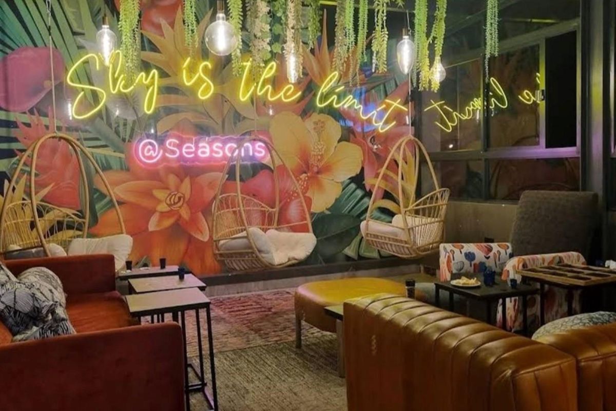 A vibrant, modern lounge area featuring a large floral mural, neon signage, and hanging basket chairs, creating a stylish and inviting atmosphere.