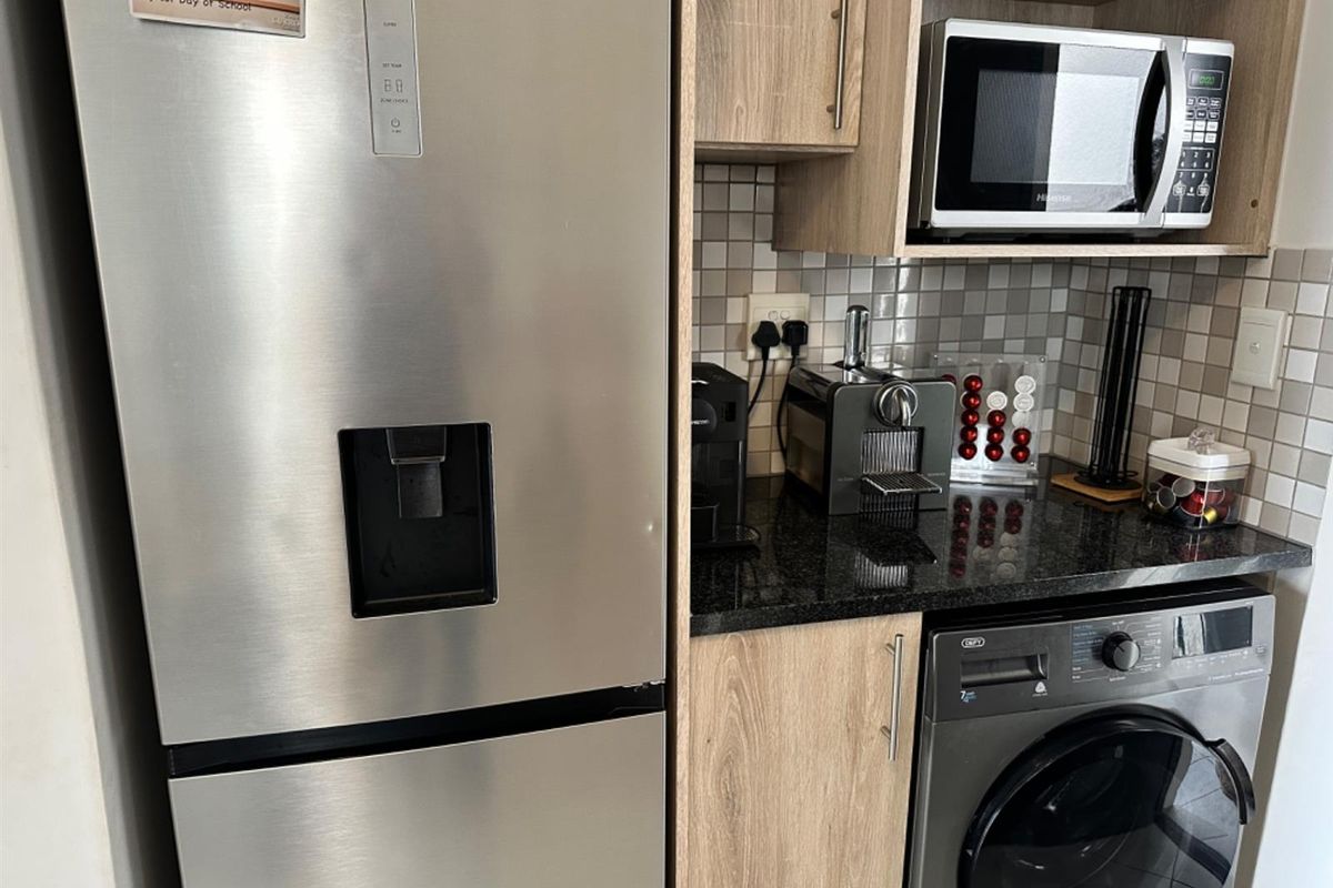 A compact kitchen area featuring modern laminate cabinetry, granite countertops, a tiled backsplash, and a built-in microwave with space for a washing machine.