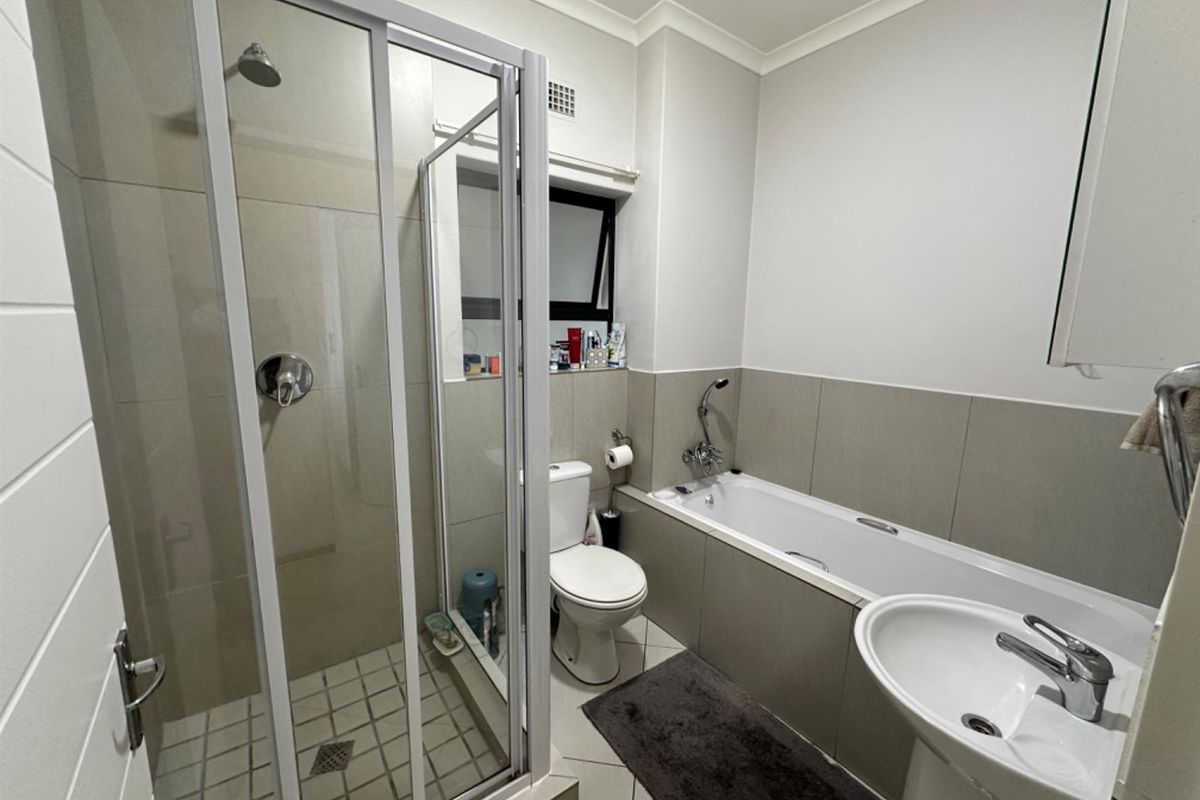 A functional bathroom featuring a separate shower enclosure, a bathtub with a handheld mixer, a pedestal basin, and neutral wall and floor tiling.