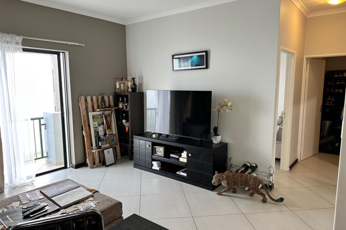 A well-lit living room featuring neutral wall tones, tiled flooring, and a sliding glass door providing access to an outdoor balcony area.