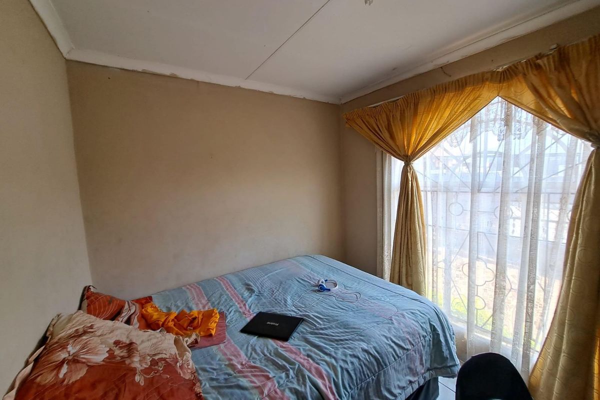 A bedroom featuring a window with security bars and standard ceiling finishes, requiring cosmetic updates to the walls and ceiling.