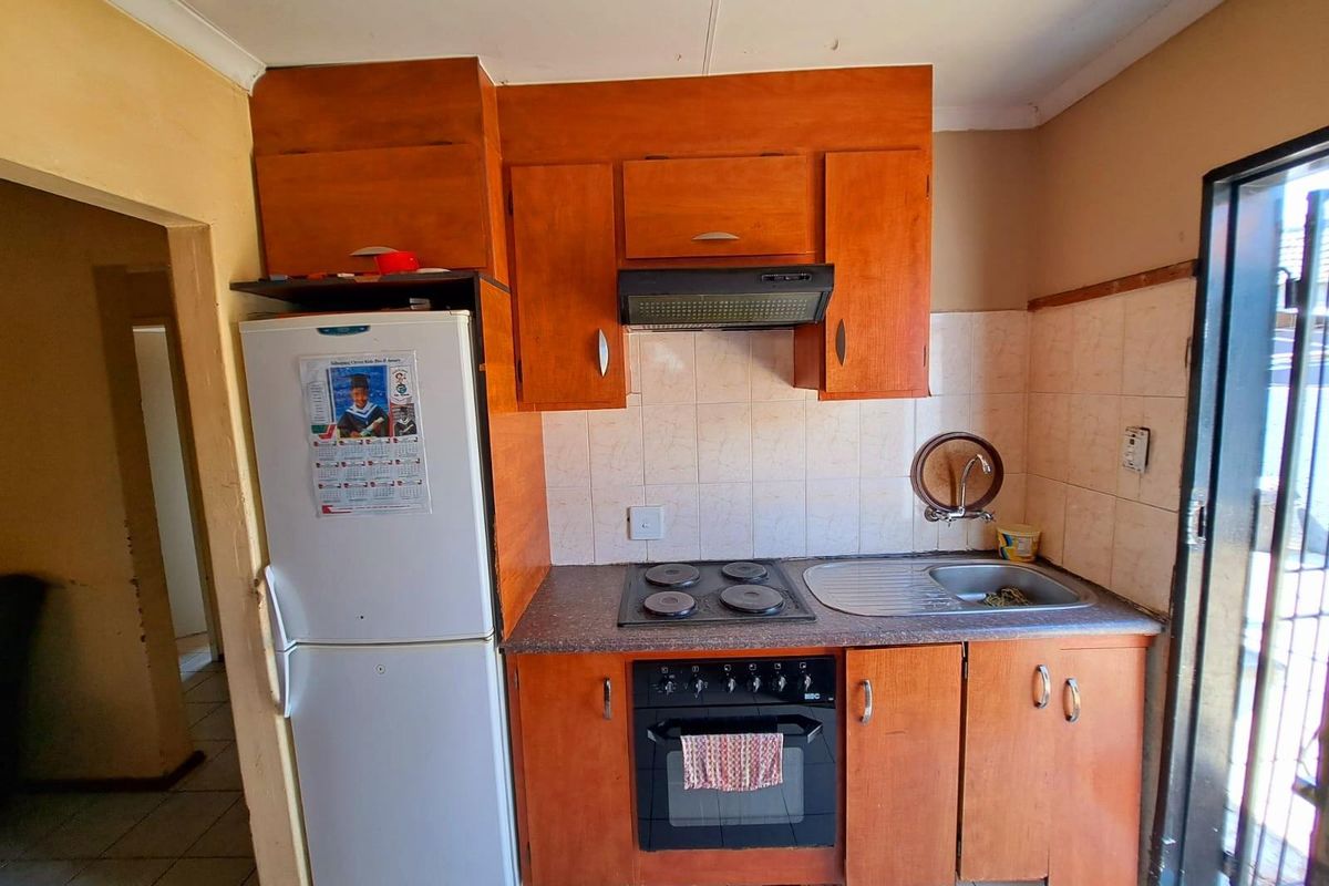 Compact kitchen featuring wooden cabinetry, a built-in oven with hob, extractor fan, and a stainless steel sink with tiled splashback.