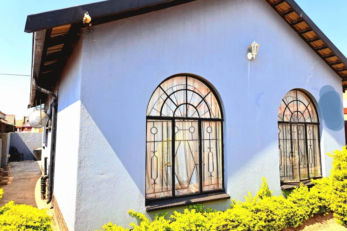 Side elevation of a residential property featuring arched windows with decorative metal security grilles and a textured blue facade.