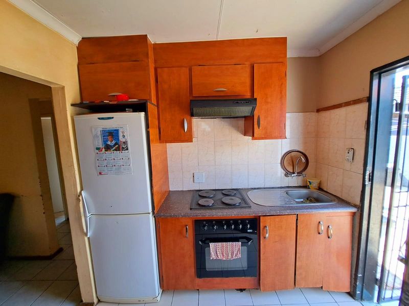 Compact kitchen featuring wooden cabinetry, a built-in oven with hob, extractor fan, and a stainless steel sink with tiled splashback.