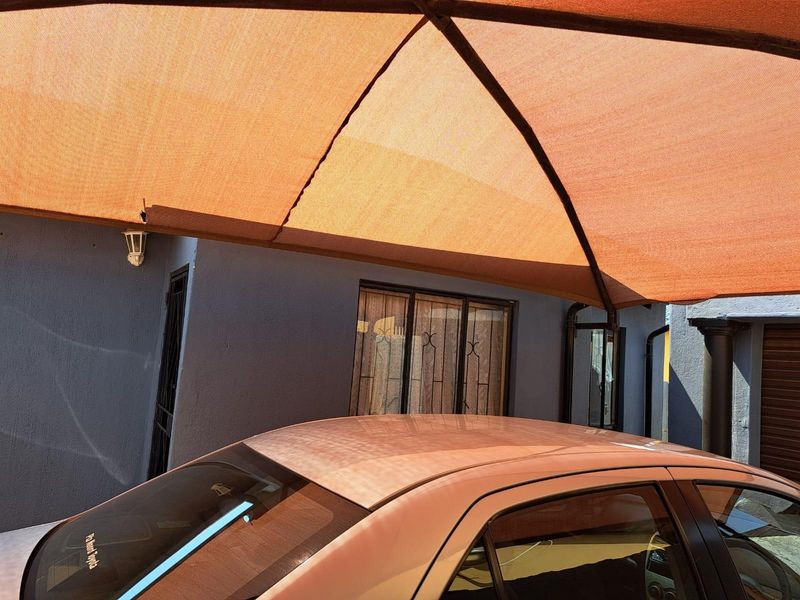 An outdoor parking area featuring a structural shade sail covering, providing protection for vehicles against the elements.