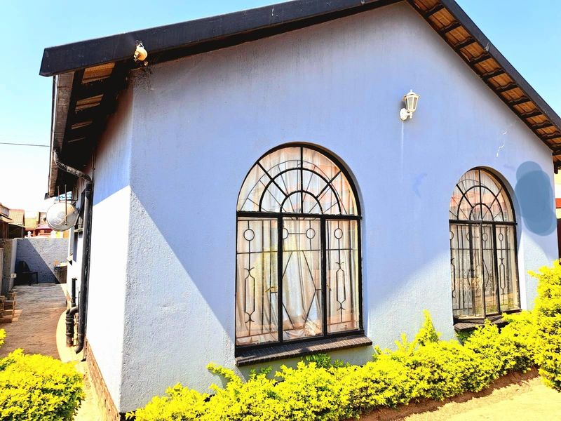 Side elevation of a residential property featuring arched windows with decorative metal security grilles and a textured blue facade.