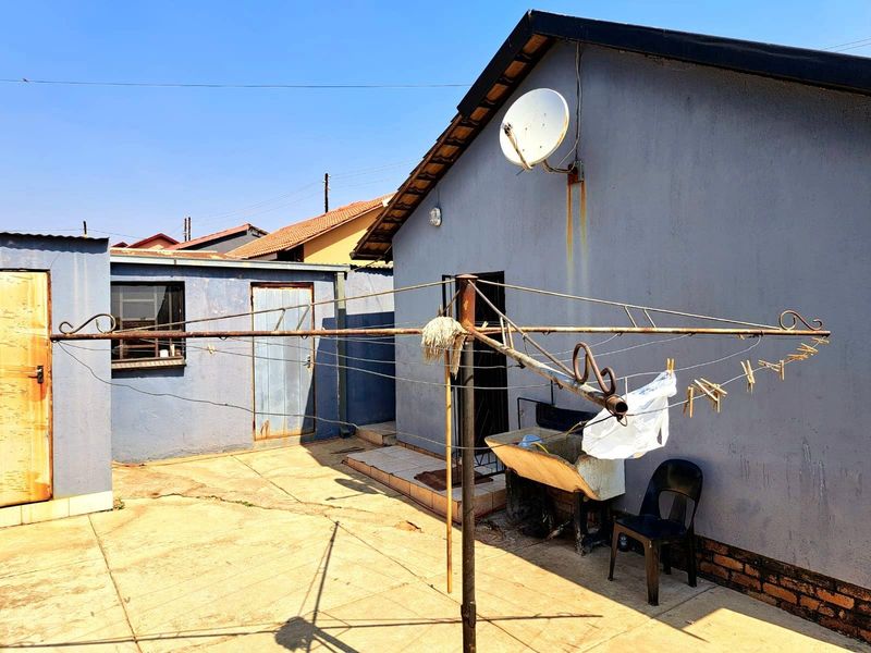 Rear exterior view of the property featuring a concrete paved courtyard, utility area, and wall-mounted satellite dish.