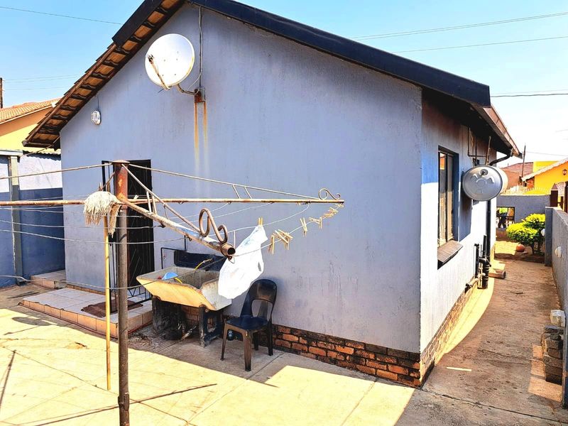 Rear exterior view of the house featuring a paved yard, external plumbing fixtures, and a satellite dish mounted on the wall.