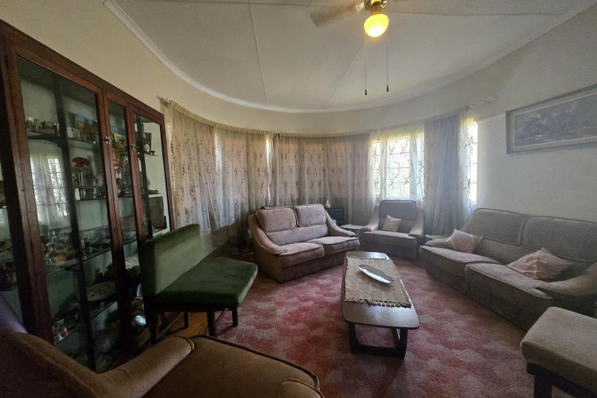 A spacious living room featuring a distinctive curved wall, coved ceiling, and a ceiling fan, offering a classic layout with significant potential for modernization.