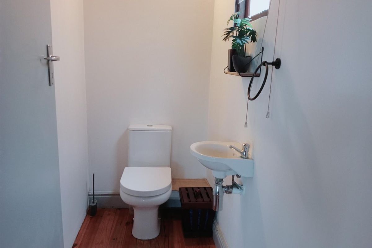 A compact guest bathroom featuring a wall-mounted basin, a standard toilet, and timber flooring.