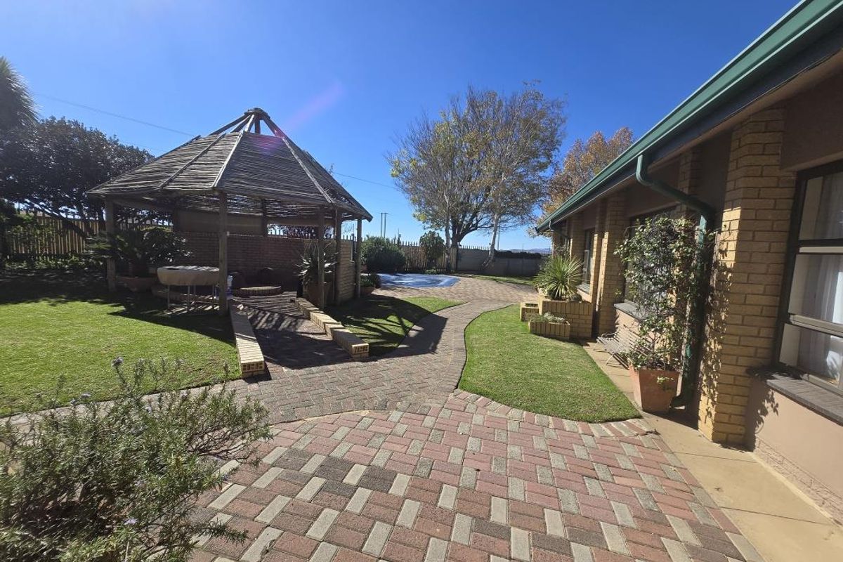 A well-maintained rear garden featuring brick paving, a wooden gazebo, a swimming pool, and established lawn areas adjacent to the brick house facade.