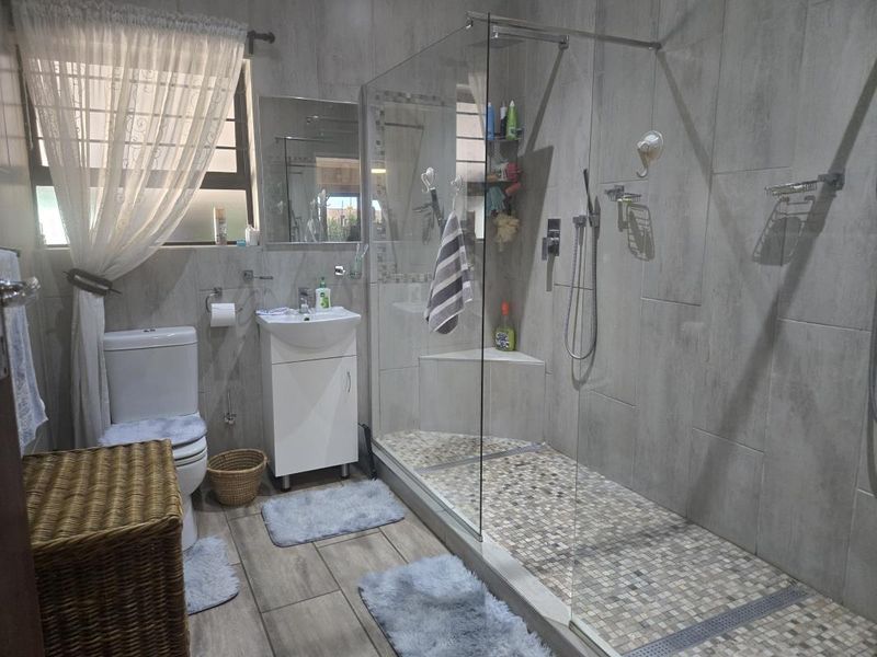 Modern bathroom featuring a spacious walk-in shower with glass enclosure, mosaic floor tiling, vanity basin, and neutral wall tiles.