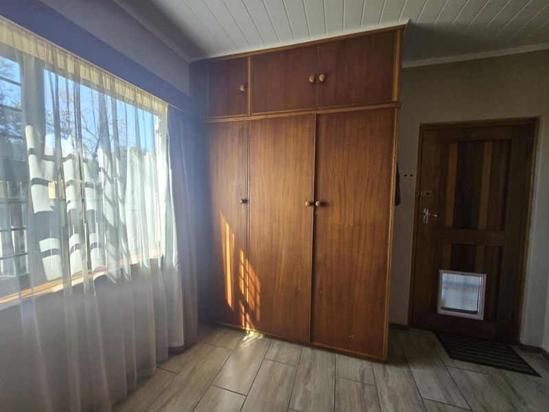A bedroom featuring built-in wooden cupboards, tiled flooring, and a timber door with an integrated pet flap.