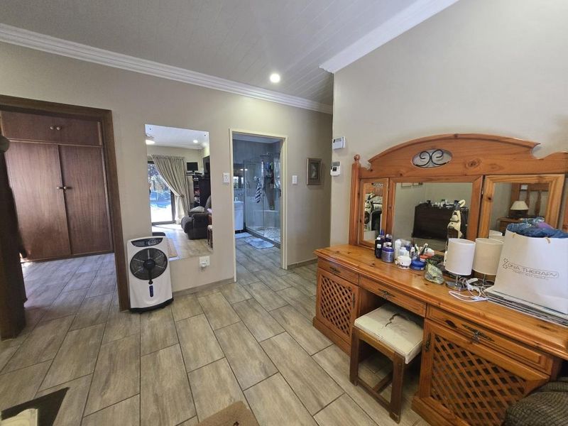 Spacious bedroom featuring tiled flooring, built-in cupboards, and direct access to an en-suite bathroom, offering a functional layout with neutral wall finishes.