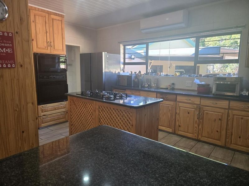 A functional kitchen featuring wooden cabinetry, granite countertops, a central island with a gas hob, and built-in oven, complemented by tiled flooring.