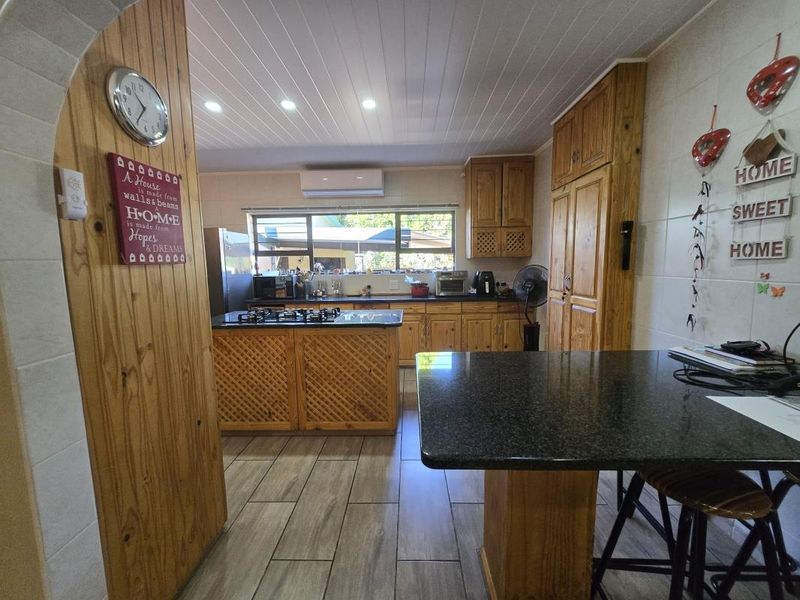 A functional kitchen featuring wooden cabinetry, granite countertops, a central island with a gas hob, and modern tiled flooring.