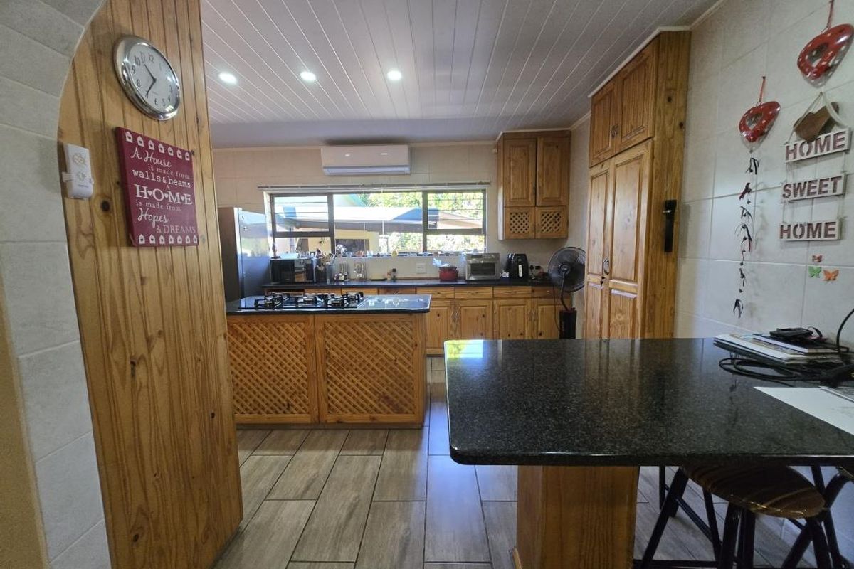 A functional kitchen featuring wooden cabinetry, granite countertops, a central island with a gas hob, and modern tiled flooring.
