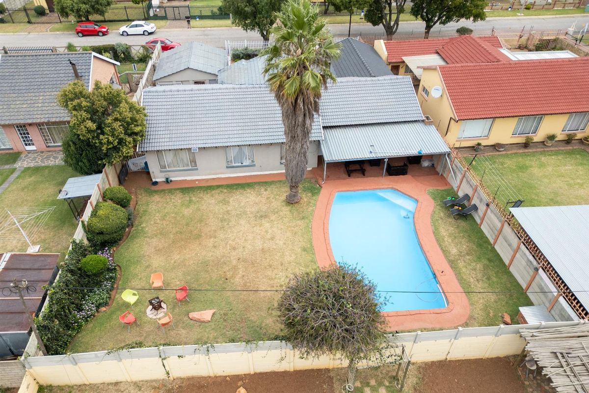 Aerial view of a residential property featuring a private swimming pool, covered patio area, and a spacious backyard with perimeter walling.