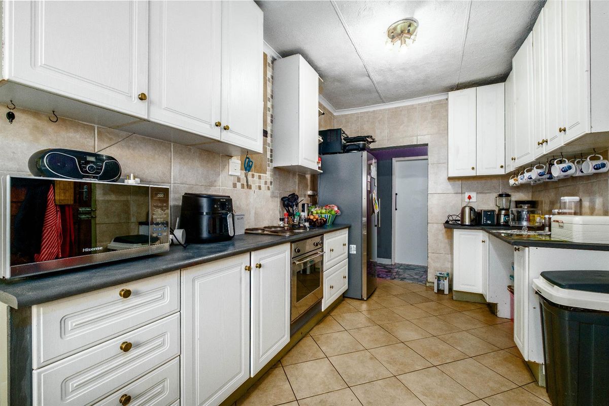 A functional kitchen featuring white cabinetry, dark countertops, tiled backsplash, and ceramic floor tiles, offering a practical layout for daily meal preparation.