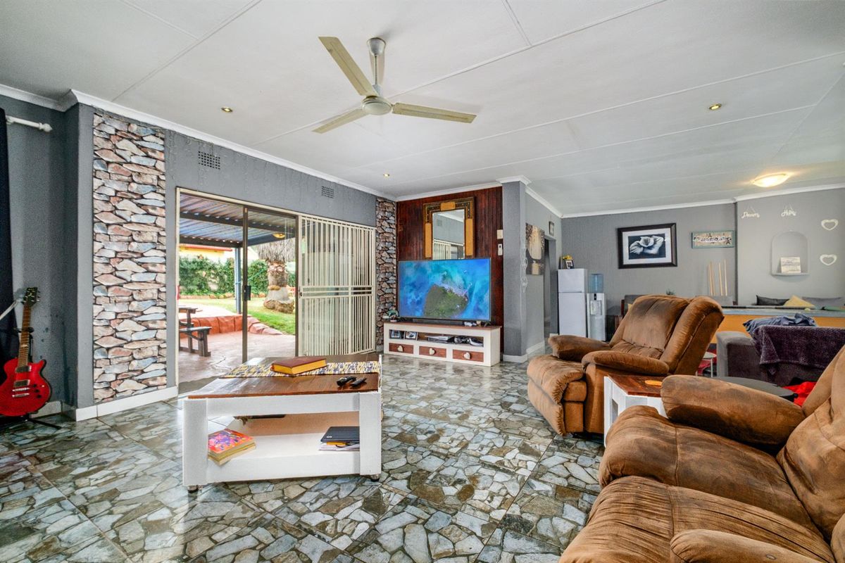Spacious living room featuring unique stone-style flooring, a ceiling fan, and sliding glass doors that open to an outdoor patio area.