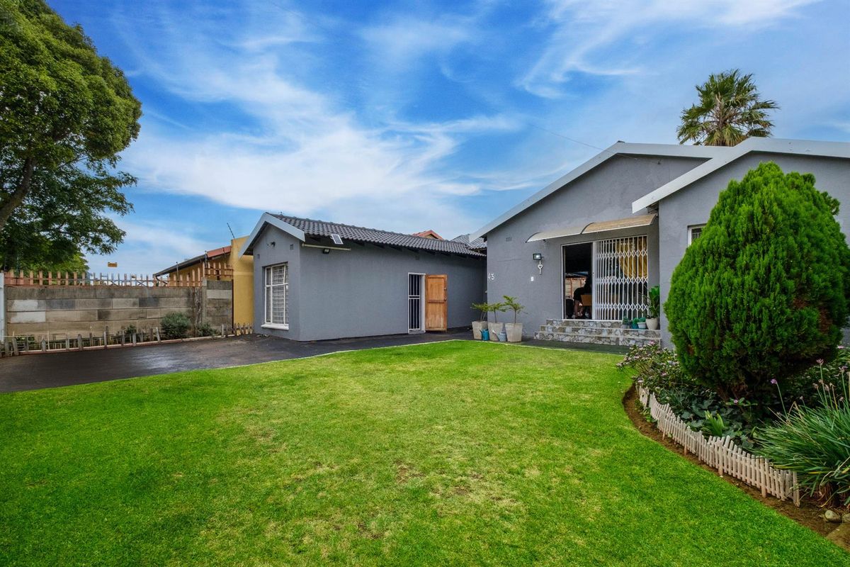A well-maintained rear exterior view featuring a spacious lawn, paved driveway, and a detached garage structure adjacent to the main house.