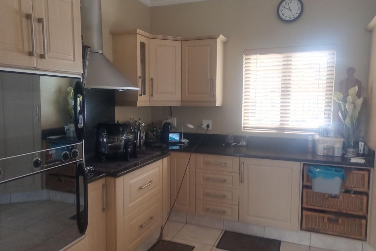 A functional kitchen featuring light-toned cabinetry, dark stone countertops, a built-in oven, and an extractor fan, with tiled flooring and natural light.