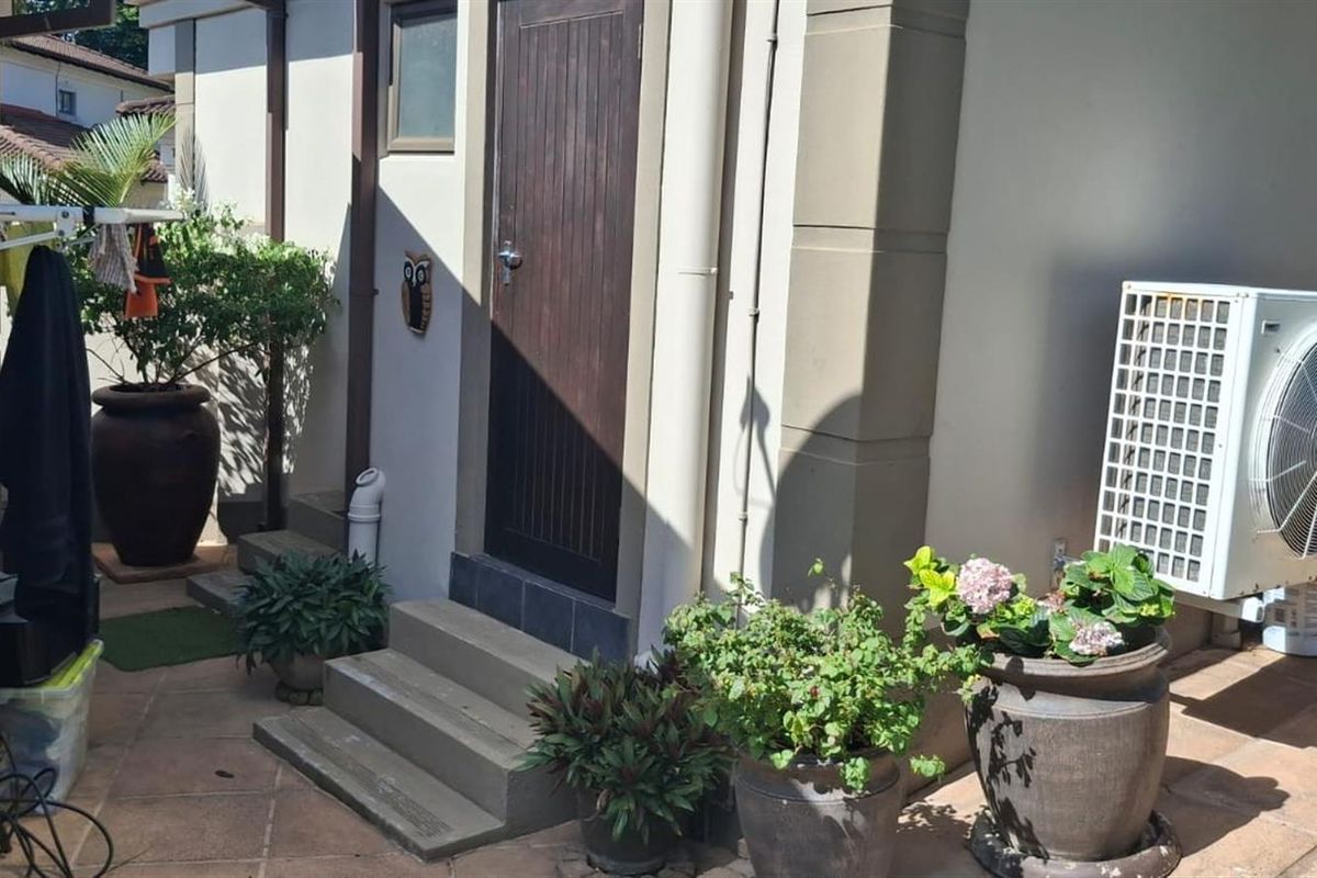 A functional rear patio area featuring tiled flooring, concrete steps, an air conditioning unit, and a water storage tank.