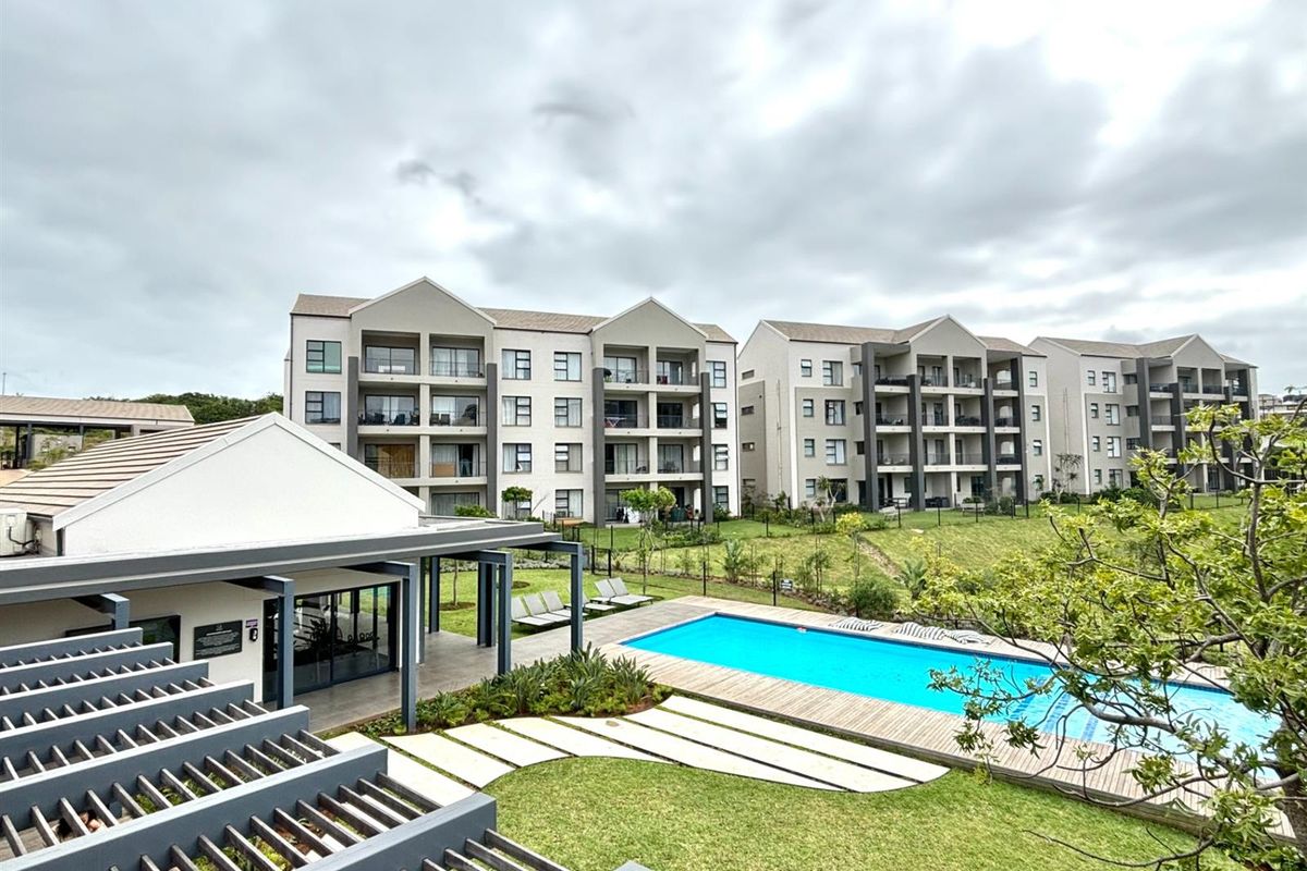 Elevated view of a modern apartment complex featuring a communal swimming pool, landscaped gardens, and covered patio areas.