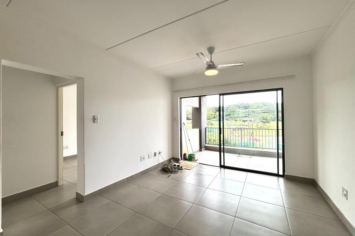 Bright and spacious living area featuring neutral floor tiles, a ceiling fan, and large sliding glass doors leading to a private balcony.