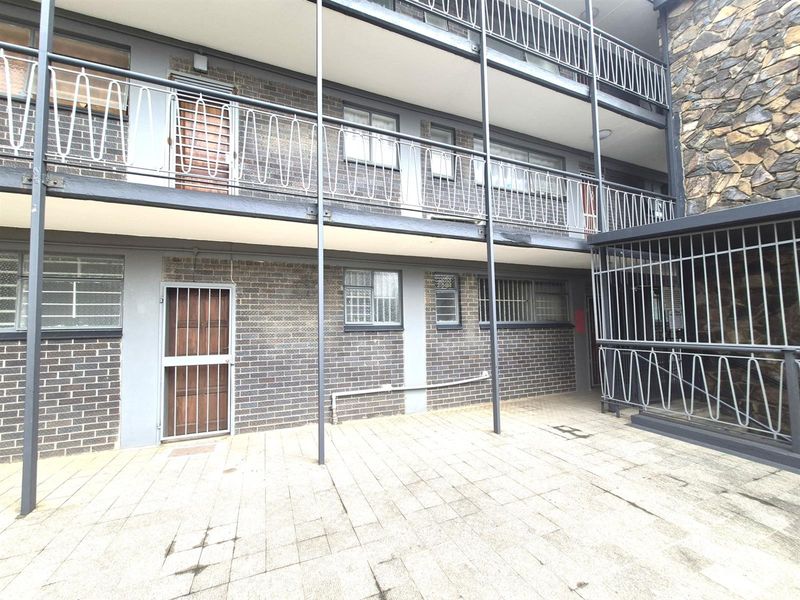 Exterior view of an apartment building featuring a paved courtyard area, multi-level balconies with metal railings, and brick facade construction.