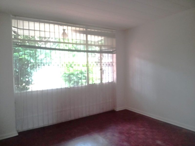 An empty bedroom featuring parquet flooring and a large window with security bars, offering a blank canvas for interior design.