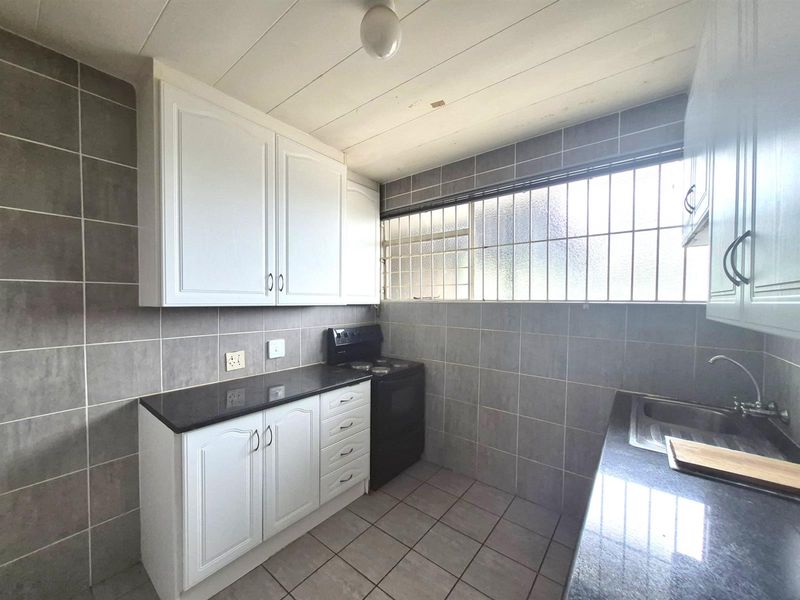 A functional kitchen featuring white cabinetry, dark granite countertops, tiled walls, and a built-in stove with a security-grilled window.