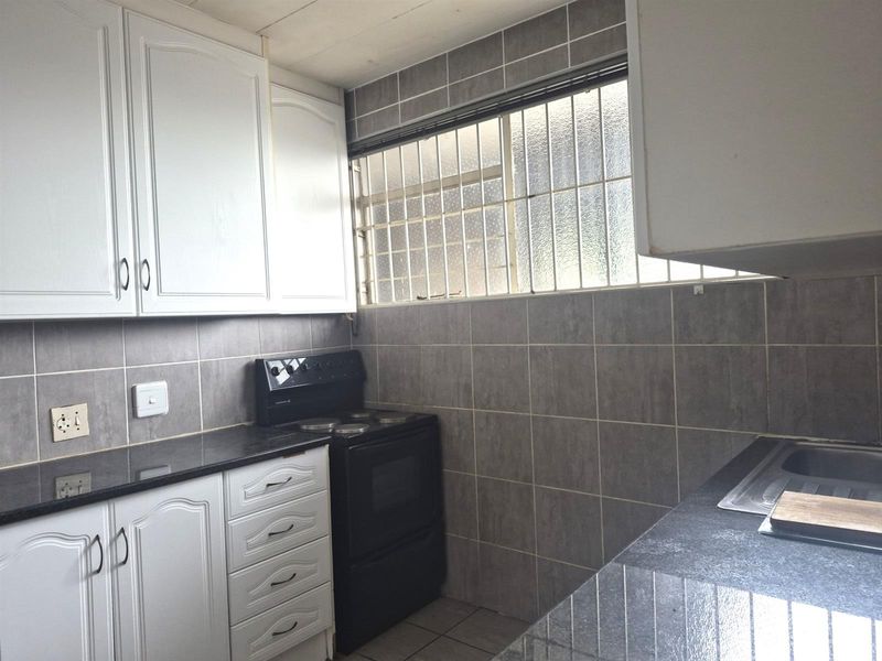 A functional kitchen featuring white cabinetry, dark countertops, a built-in stove, and tiled splashbacks with a security-grilled window.