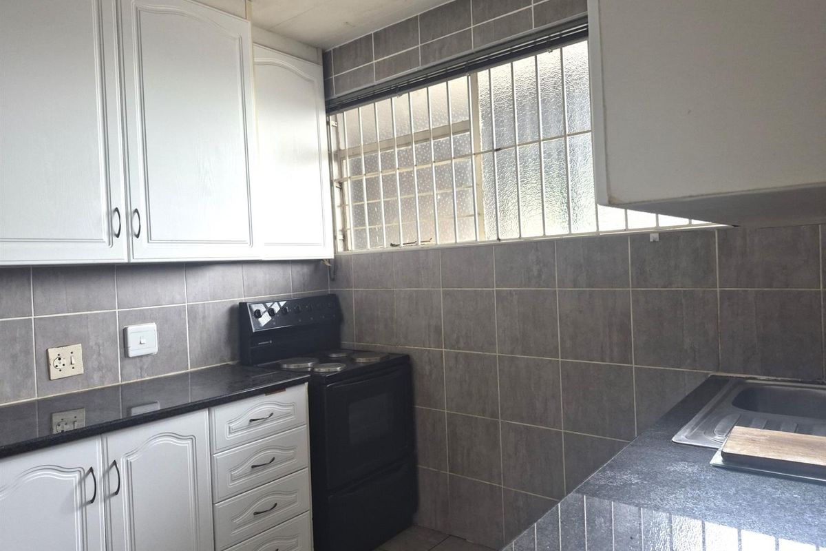 A functional kitchen featuring white cabinetry, dark countertops, a built-in stove, and tiled splashbacks with a security-grilled window.