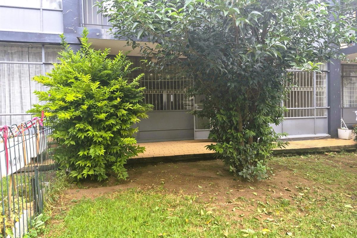 Ground floor apartment exterior featuring a paved patio area, security gates, and a small private garden space.
