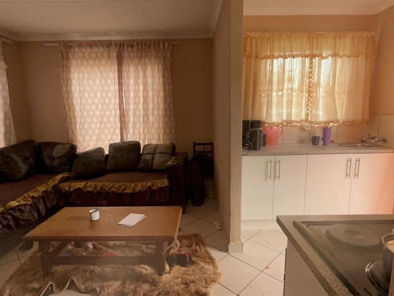 An open-plan living and kitchen area featuring tiled flooring, built-in kitchen cabinetry, and a functional layout connecting the lounge and cooking space.