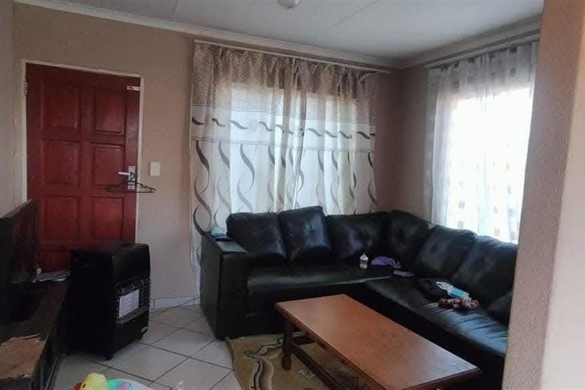 A functional living area featuring tiled flooring, neutral wall tones, and natural light through window treatments, providing a comfortable space for relaxation.