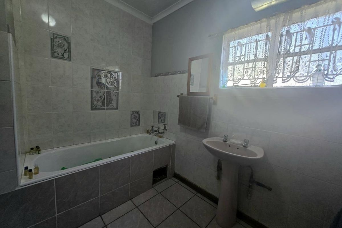 A functional bathroom featuring a built-in bathtub, pedestal washbasin, and neutral ceramic wall and floor tiling.