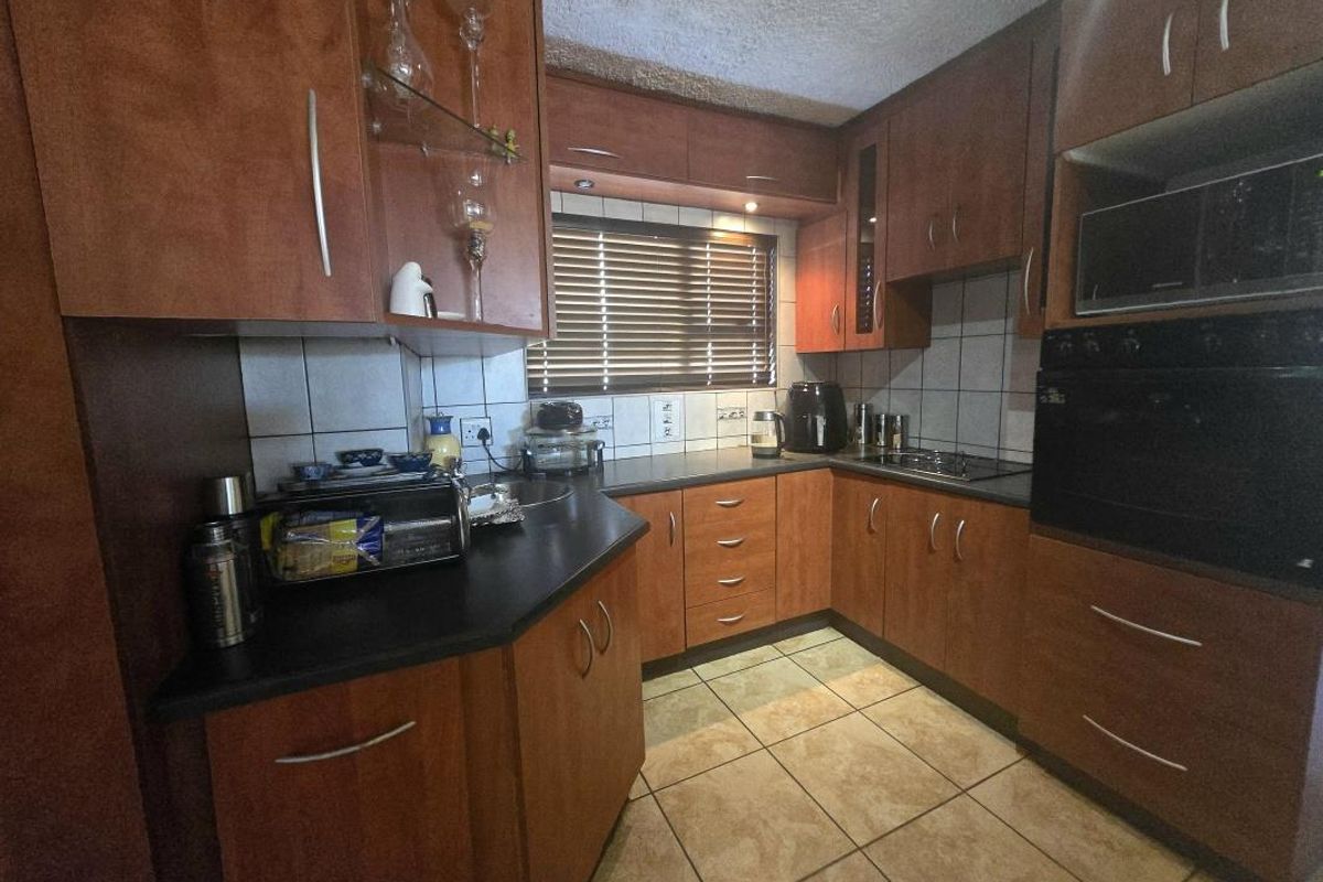 A functional kitchen featuring wooden cabinetry, laminate countertops, built-in oven and microwave, tiled backsplash, and ceramic floor tiles.