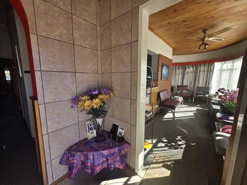 A commercial waiting area featuring tiled wall accents, a timber ceiling with a fan, and large windows allowing natural light into the space.