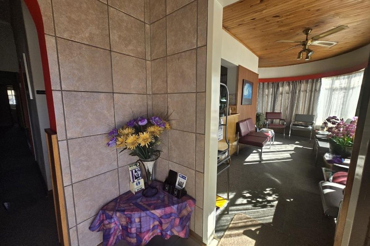 A commercial waiting area featuring tiled wall accents, a timber ceiling with a fan, and large windows allowing natural light into the space.