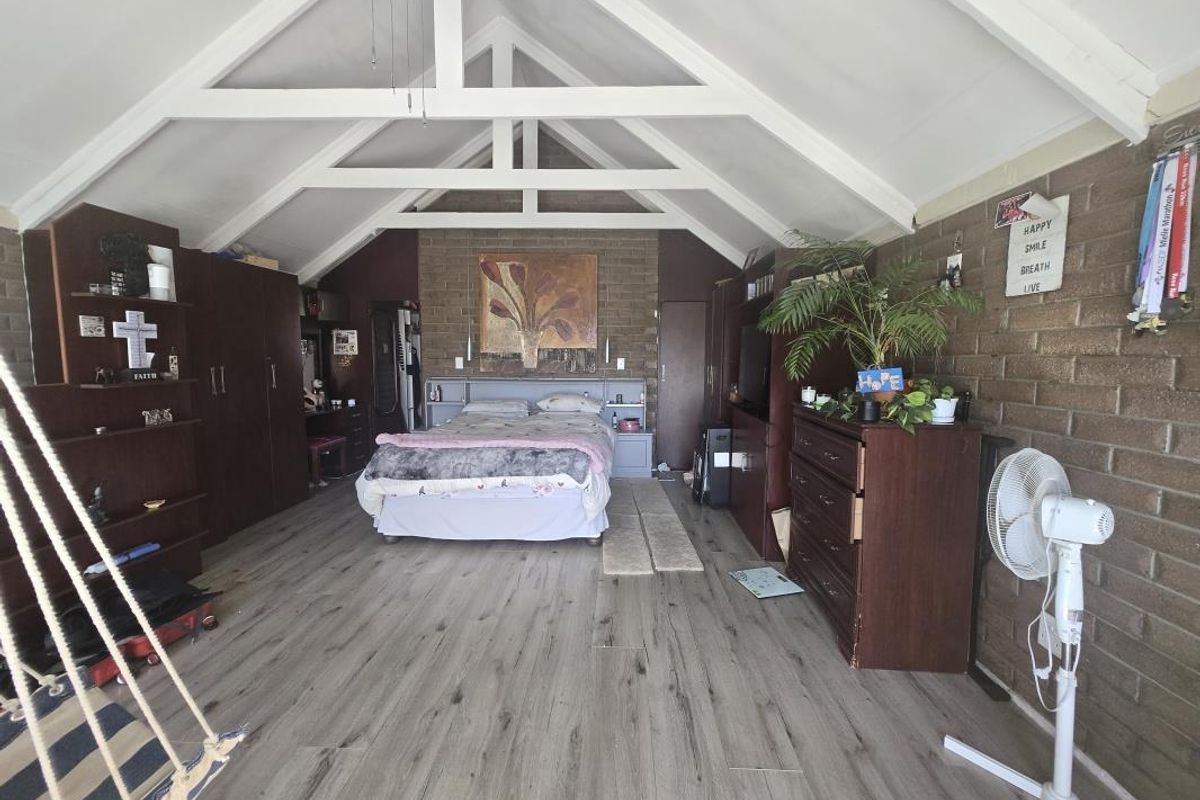 Spacious bedroom featuring a high vaulted ceiling with exposed timber trusses, laminate flooring, and an exposed brick feature wall with built-in storage.