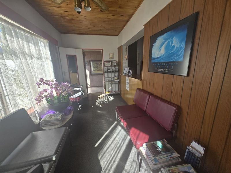 A commercial reception area featuring wood-paneled walls, a timber ceiling, and a built-in reception counter, currently utilized as a waiting room.