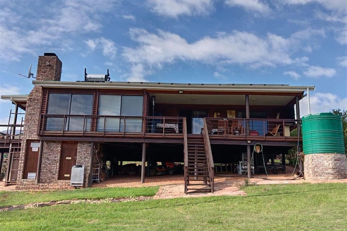 Rear view of a raised farm-style dwelling featuring a large covered timber deck, brick chimney, and an elevated living area with sliding glass doors.